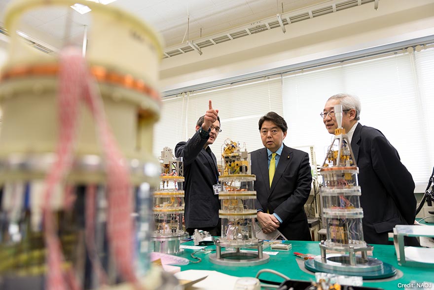 アルバロ・ゴンザレス准教授(左)と常田国立天文台長(右)からアルマ受信機の開発について説明を受けている林文部科学大臣(中央)