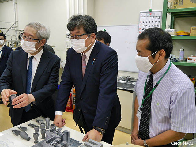 写真：金属3Dプリンターで作成された部品について説明を受ける萩生田文部科学大臣（中央）。