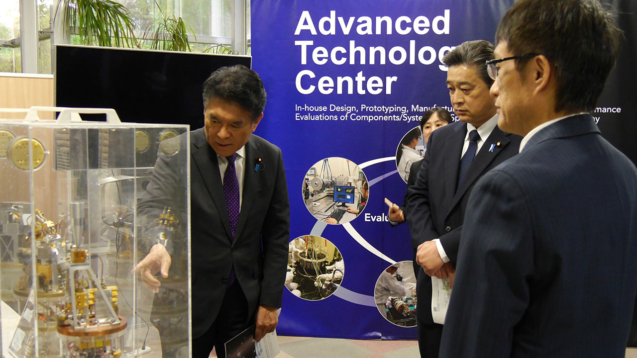 先端技術センターにて、井口教授より観測機器の製作技術について説明を受ける小林文部科学副大臣（左）と清水文部科学大臣政務官（中央）。